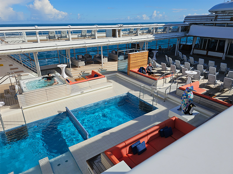 The spacious pool area on Deck 8 includes a heated swimming pool, water loungers, a whirlpool, and a bar